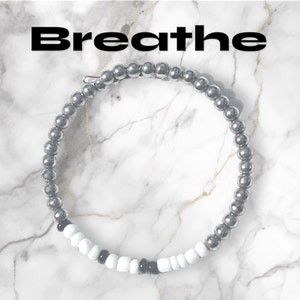 May include: A silver beaded bracelet with black and white beads spelling out the word "Breathe".