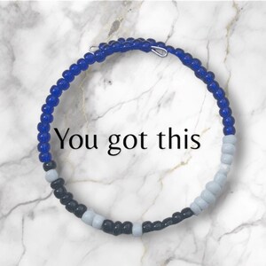 May include: A blue, white, and black beaded bracelet with the text "You got this" on a white marble background.