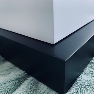 May include: A white box sits on top of a black box. Both boxes are made of wood and have a smooth, polished finish.