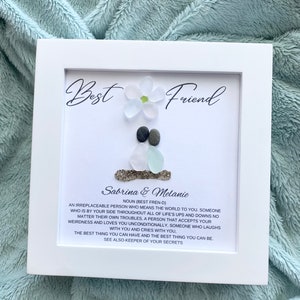 May include: White framed artwork with a sea glass flower and two pebbles. The text reads "Best Friend" and "Sabrina & Melanie" with a definition of the word "friend".