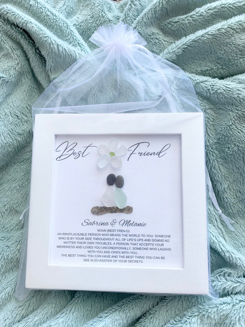 May include: White framed artwork with a sea glass and shell design. The artwork features the text "Best Friend" and "Sabrina & Melanie". The text below the names reads "An irreplaceable person who means the world to you..."