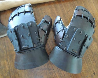 May include: A pair of brown leather gauntlets with black leather accents and stitching. The gauntlets have a segmented design and are secured with straps.