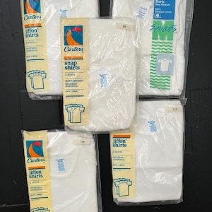 Puede incluir: Un conjunto de cinco paquetes de camisetas interiores para beb&eacute;s y ni&ntilde;os peque&ntilde;os de la marca Carter's. Los paquetes son blancos con detalles azules y rojos. Cada paquete contiene dos camisetas y est&aacute; etiquetado con la talla y el tipo de camiseta. Las camisetas est&aacute;n hechas de 100% algod&oacute;n.