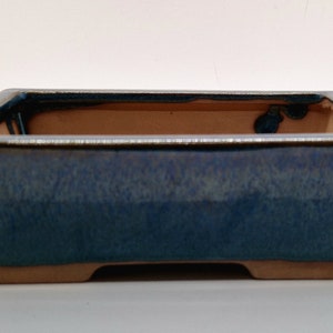May include: A rectangular blue ceramic bonsai pot with a glazed finish. The pot has a slightly raised rim and a flat base.