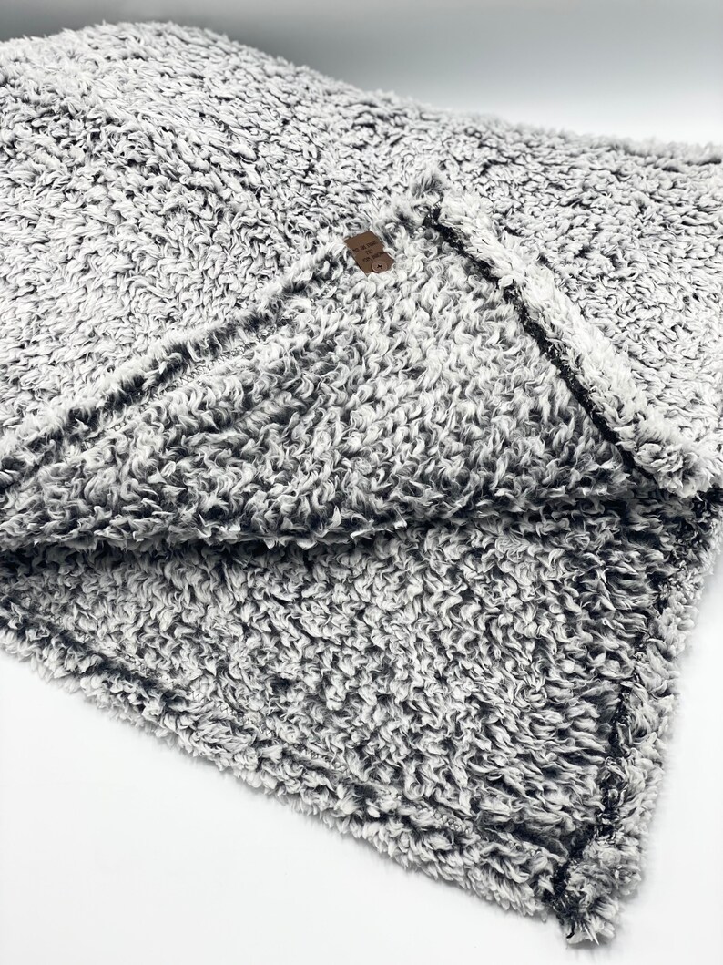 May include: A soft, gray and white fuzzy blanket with a black trim. The blanket is folded in half and the tag is visible.