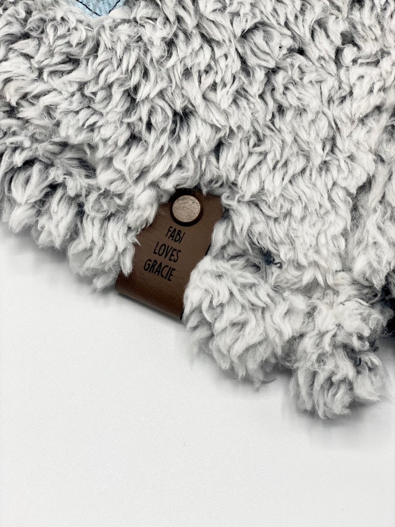 May include: A brown leather tag with the text "Fabi Loves Gracie" attached to a gray fuzzy blanket.