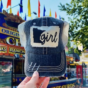 May include: A black and white trucker hat with a white patch featuring the outline of the state of Minnesota and the word "girl" in black script.