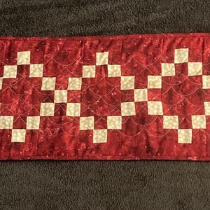 May include: A red table runner with a white geometric pattern. The pattern is made up of squares and circles.