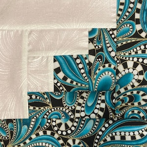 May include: A quilt block with a white background and a blue and black patterned design. The pattern features swirls and dots.