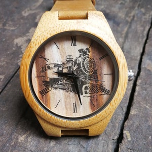 May include: A wooden wristwatch with a brown leather strap. The watch face features a black and white image of a steam locomotive with Roman numeral hour markers.