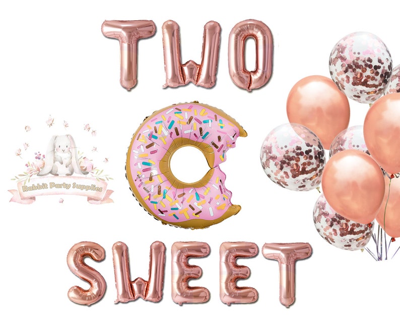 Op de afbeelding: Rosegouden folieballonnen met de tekst "TWO SWEET" en een donutvormige ballon met kleurrijke hagelslag. Er zijn ook verschillende roze en met confetti gevulde ballonnen, ideaal voor een tweede verjaardag.