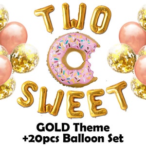 Op de afbeelding: Een gouden ballonnenset voor een verjaardagsfeest. De set bevat gouden folieballonnen met de tekst "TWO SWEET" en een donutvormige ballon. Extra ballonnen zijn roze en transparant met gouden confetti. De tekst "GOLD Theme +20pcs Balloon Set" is ook inbegrepen.