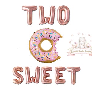 Op de afbeelding: Ros&eacute;gouden folieballonnen met de tekst "TWO SWEET" en een roze donutballon met hagelslag. Er is een hap uit de donut genomen. Een logo met een konijn en de woorden "Rabbit Party Supplies" is ook zichtbaar.