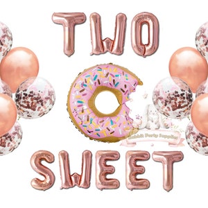 Op de afbeelding: Een verzameling feestballonnen in roze en ros&eacute;goud. De opstelling bevat de woorden "TWO SWEET" in folieballonnen, een donutvormige ballon en met confetti gevulde ballonnen. Perfect voor een tweede verjaardag.