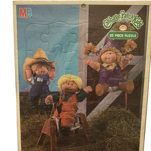 May include: A vintage Cabbage Patch Kids 25-piece puzzle featuring three Cabbage Patch Kids dolls in a barn setting. The dolls are wearing cowboy hats and clothing. The puzzle box is brown with a blue and white background. The text "Cabbage Patch Kids" and "25 Piece Puzzle" is printed on the box.