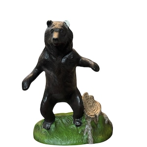 Może przedstawiać: Figurka brązowego niedźwiedzia stojąca na zielonej, trawiatej podstawie z pniem drzewa. Niedźwiedź ma wyciągnięte ramiona, a figurka jest szczegółowa z fakturą futra. Podstawa ma około 10 cm długości.