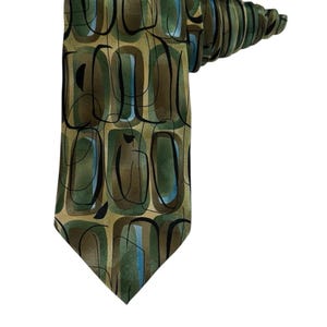 May include: A necktie featuring a repeating pattern of rounded rectangular shapes in shades of olive green, brown, and light blue, overlaid with thin, black, hand-drawn style circular lines on a smooth, slightly reflective fabric surface.