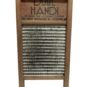 Op de afbeelding: Vintage houten wasbord met een gegolfd metalen schrobvlak. Het bovenste gedeelte toont de tekst "DUBL HANDI" en "COLUMBUS WASHBOARD CO., COLUMBUS, O". Het wasbord heeft een rechthoekige vorm met vier poten.
