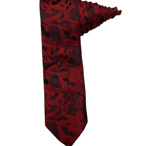 May include: A red silk tie with a repeating pattern of Mickey Mouse heads. The tie is folded and tied in a knot.