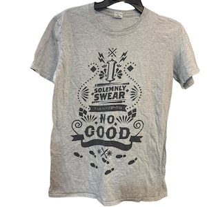 以下が含まれることがあります： 黒いグラフィックデザインのグレーのTシャツ。デザインには「Solemnly Swear I Am Up To No Good」という言葉と足跡が含まれています。Tシャツは黒いハンガーに吊るされています。