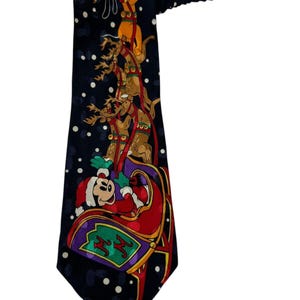 Puede incluir: Una corbata de seda azul oscuro con un tema navideño que presenta a Mickey Mouse y Pluto en un trineo tirado por renos. El fondo es azul oscuro con lunares blancos.