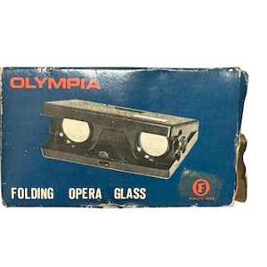 May include: A vintage Olympia Folding Opera Glass in its original box. The box is a dark blue with the word "OLYMPIA" in red at the top. The opera glasses are black and have white lenses. The box has some wear.