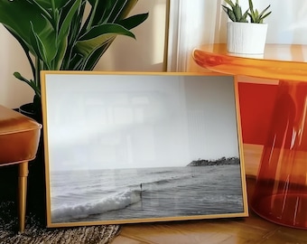 May include: A black and white photograph of a surfer riding a wave in the ocean. The photo is framed in a gold frame and is hanging on a wall.