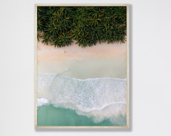 May include: An aerial view of a tropical beach with white sand, turquoise water, and lush green palm trees. The waves are crashing on the shore, creating a beautiful scene.