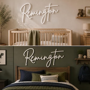 May include: A white script wall sign displaying the name Remington in a cursive font. The sign is shown in two different room settings: one above a wooden crib against a beige wall and one above a wooden bed against a dark olive green wall.