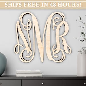 May include: A wooden monogram featuring the letters N, M, and R in a decorative script font. The letters are light-colored and mounted on a light gray wall. The image includes decorative vases and a stack of books on a dark gray surface.