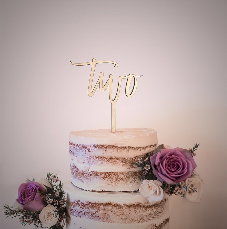 May include: A two-tiered cake decorated with flowers and a wooden cake topper that says "two" in cursive.