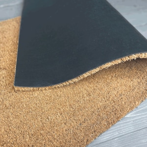 May include: A brown coir doormat with a black rubber backing. The mat is folded in half, showing the backing.