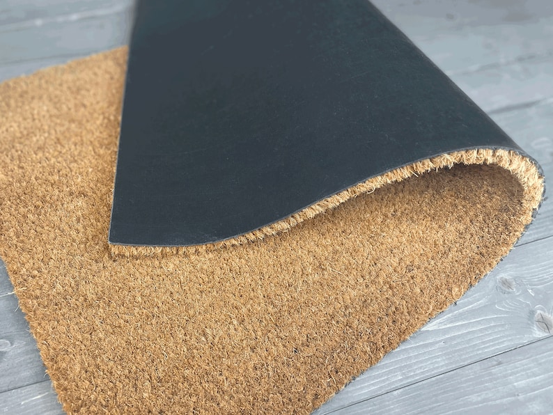 May include: A brown coir doormat with a black rubber backing. The mat is folded in half, showing the backing.