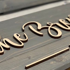 Puede incluir: Un letrero de madera con las palabras "The Brown" en escritura cursiva y "EST" debajo. El letrero est&aacute; pintado de color gris oscuro y las letras son de color madera claro.