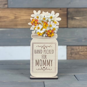 May include: Wooden cutout of a mason jar with a bouquet of white and yellow flowers. The jar has the text "HAND PICKED FOR MOMMY" on it.