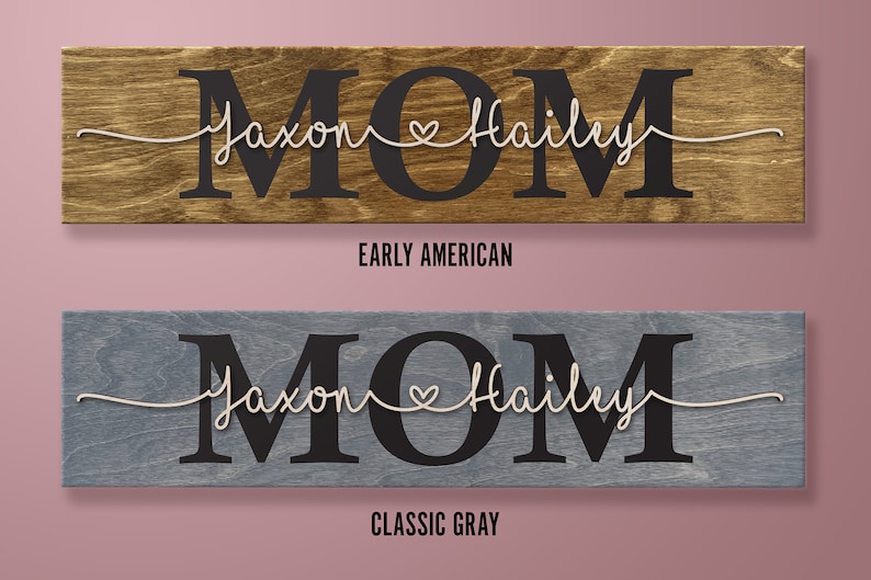 May include: Wooden sign with the word "MOM" in large black letters. The names "Jaxon" and "Hailey" are written in cursive with a heart between them. The sign is available in two colors: Early American and Classic Gray.