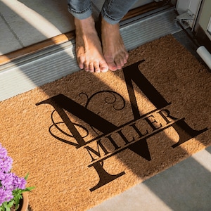 May include: A brown coir doormat with the letter "M" in a black script font. The name "Miller" is written in a smaller font below the letter "M".