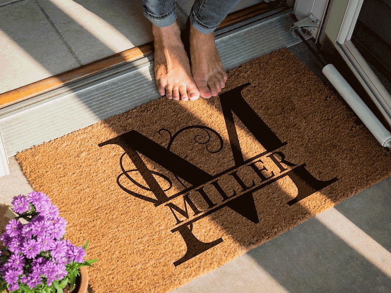 May include: A brown coir doormat with the letter "M" in a black script font. The name "Miller" is written in a smaller font below the letter "M".