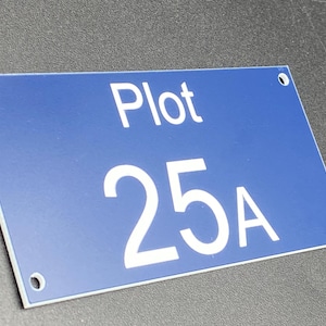 May include: A rectangular blue sign with the word "Plot" above the numbers "25A" in white. The sign has four holes, one in each corner. The sign is likely for a property or land identification.