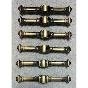 以下が含まれることがあります： 装飾的なデザインが施されたアンティークブラスのキャビネットドアプル6個。プルはすべて同じサイズと形であり、わずかに経年変化した仕上げが施されています。