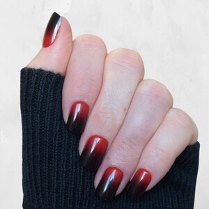 Squoval shaped nails in an Ombre design that moves from black at the tips to Cherry Red at the base. The top of the nails are a rounded square. They are a short to medium length. The nails are applied with glue or glue tab application.