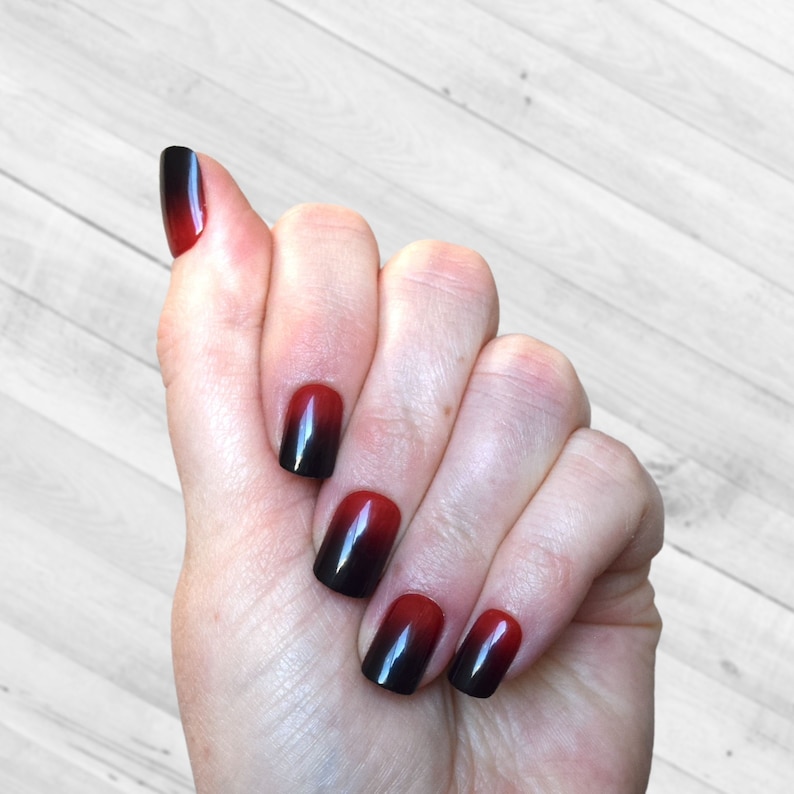 Squoval shaped nails in an Ombre design that moves from black at the tips to Cherry Red at the base. The top of the nails are a rounded square. They are a short to medium length. The nails are applied with glue or glue tab application.