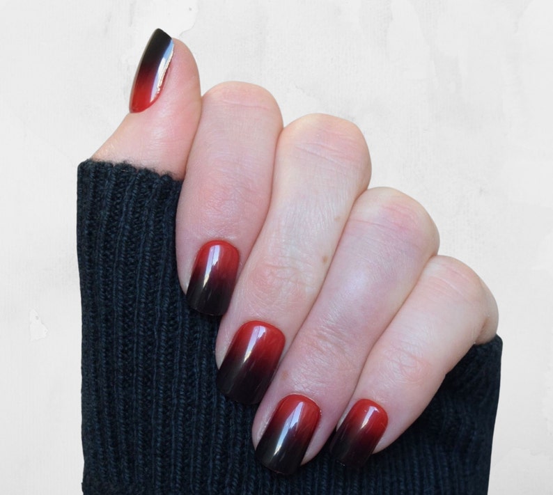 Squoval shaped nails in an Ombre design that moves from black at the tips to Cherry Red at the base. The top of the nails are a rounded square. They are a short to medium length. The nails are applied with glue or glue tab application.