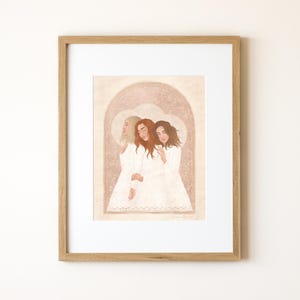 May include: A framed illustration of three women with long hair, wearing white dresses, standing together in a soft pink and white archway. The women are looking down and their hair is flowing. The illustration is in a light brown frame.
