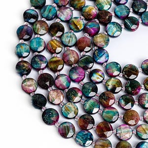 May include: A close-up of a necklace made of faceted, round beads. The beads are a mix of colors, including teal, purple, brown, and gold. The beads are strung together with a clear string, creating a beautiful and unique piece of jewelry.