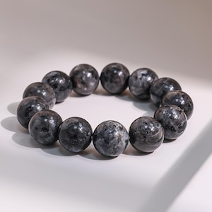 May include: A bracelet composed of spherical beads in shades of grey. The beads have a marbled appearance with lighter grey and white inclusions. The bracelet is presented on a white background.
