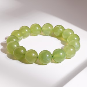 May include: A light green beaded bracelet. The bracelet is made of large, round beads strung together. The beads have a translucent quality, and the color is a soft, muted green. The bracelet is displayed on a white surface.