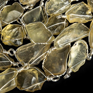 Puede incluir: Primer plano de un collar hecho con piedras preciosas crudas, transparentes y teñidas de amarillo, envueltas en alambre de plata. Las piedras preciosas tienen una forma irregular y una textura natural y rugosa.