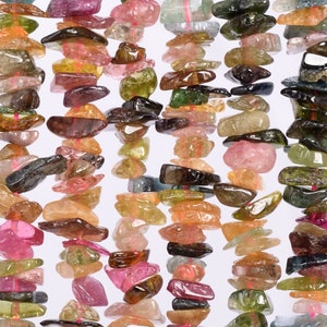 May include: Strands of colorful tourmaline gemstone chips in shades of pink, green, brown, and clear. The chips are irregularly shaped and strung together with pink thread, creating a textured and vibrant appearance. Ideal for jewelry making.