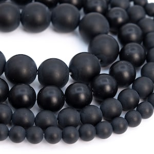 May include: A close-up of a strand of black matte beads. The beads are round and smooth, and they are arranged in a circular pattern. The beads are of varying sizes, with the largest beads in the center of the circle and the smallest beads on the outside.